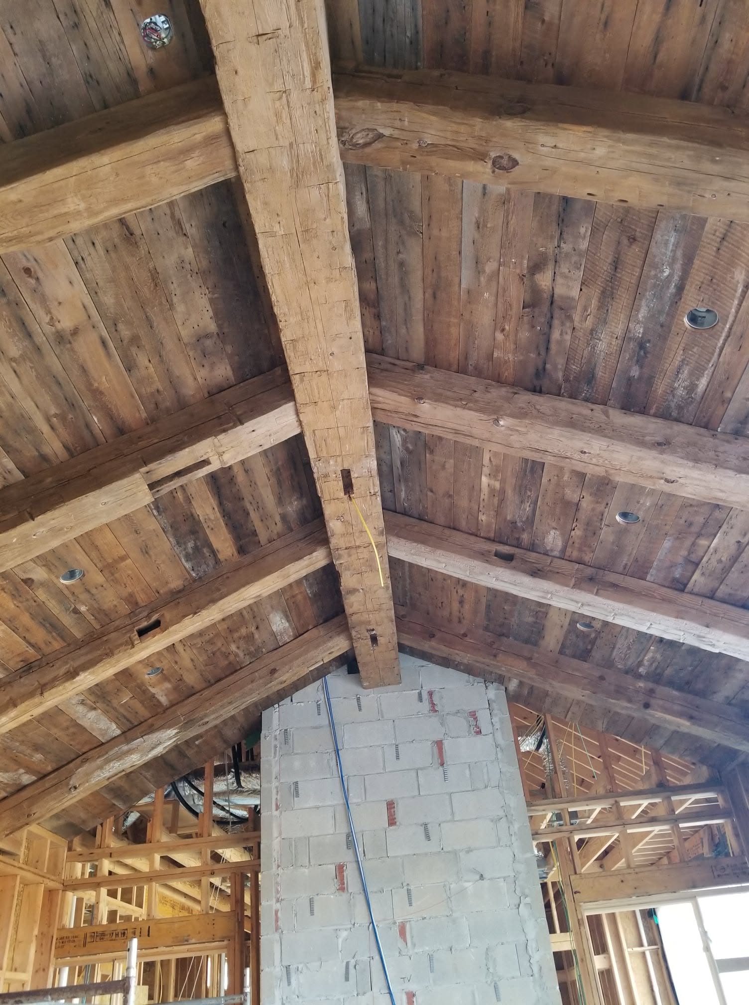 Reclaimed wood ceiling and heavy beams above an unfinished fireplace